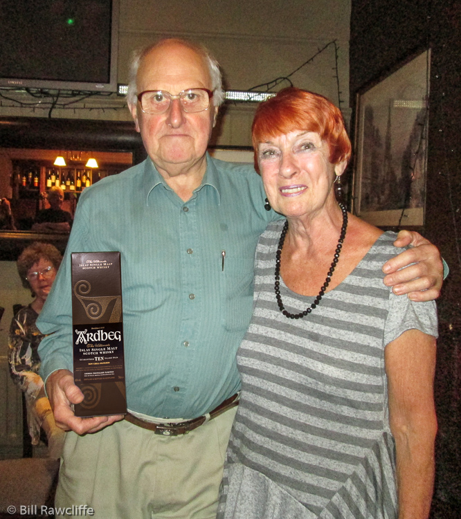 Bill Rawcliffe with Ardbeg whisky gift from Sheila Hawksworth & Natter 'n' Nibblers. (Jean Rawcliffe in background left)