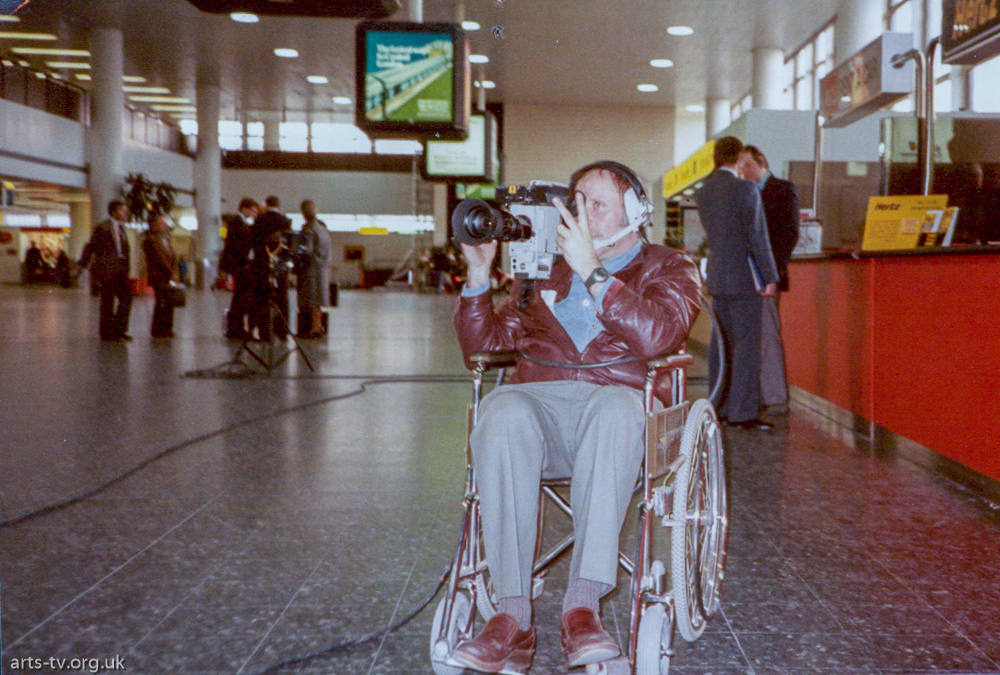 Mike Hobbs on camera in wheelchair, London Airport (?)
